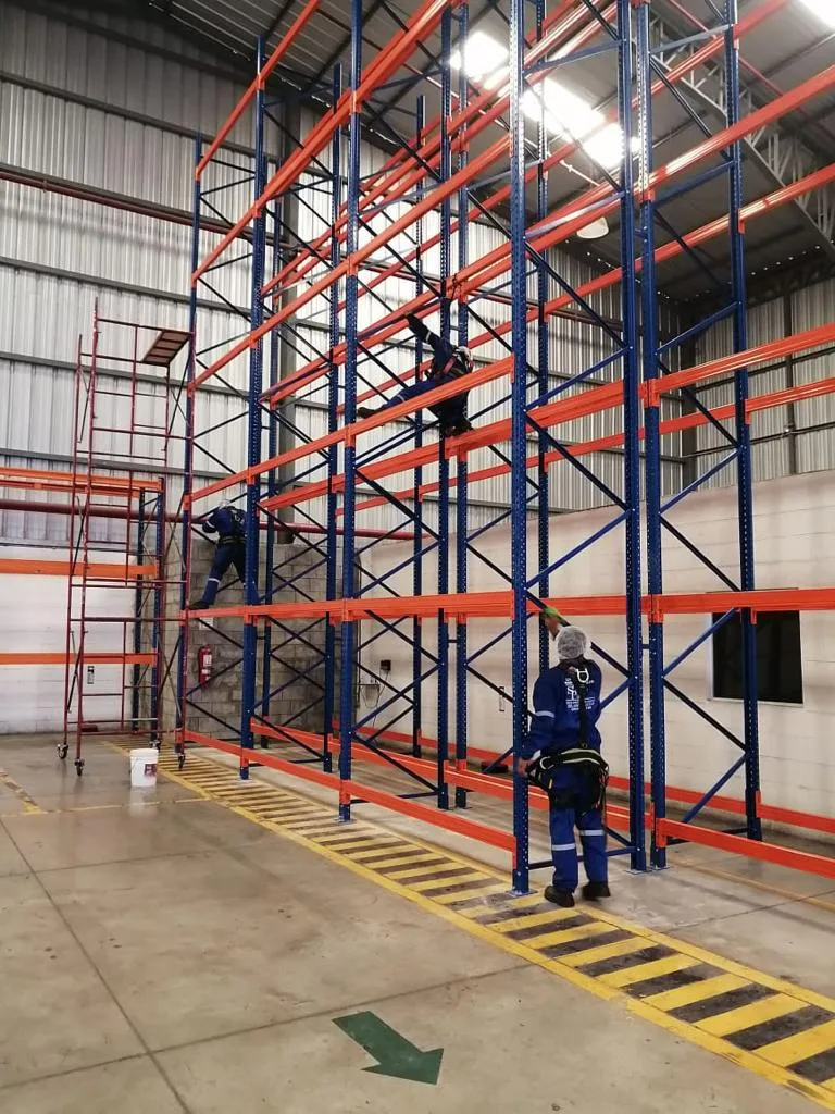 Técnicos de SolutionPlus con arnés de seguridad limpiando racks altos de una bodega