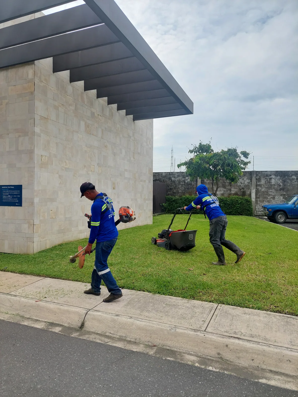 Dos técnicos de SolutionPlus con cortadora y desbrozadora dando mantenimiento al área verde de la entrada de un complejo