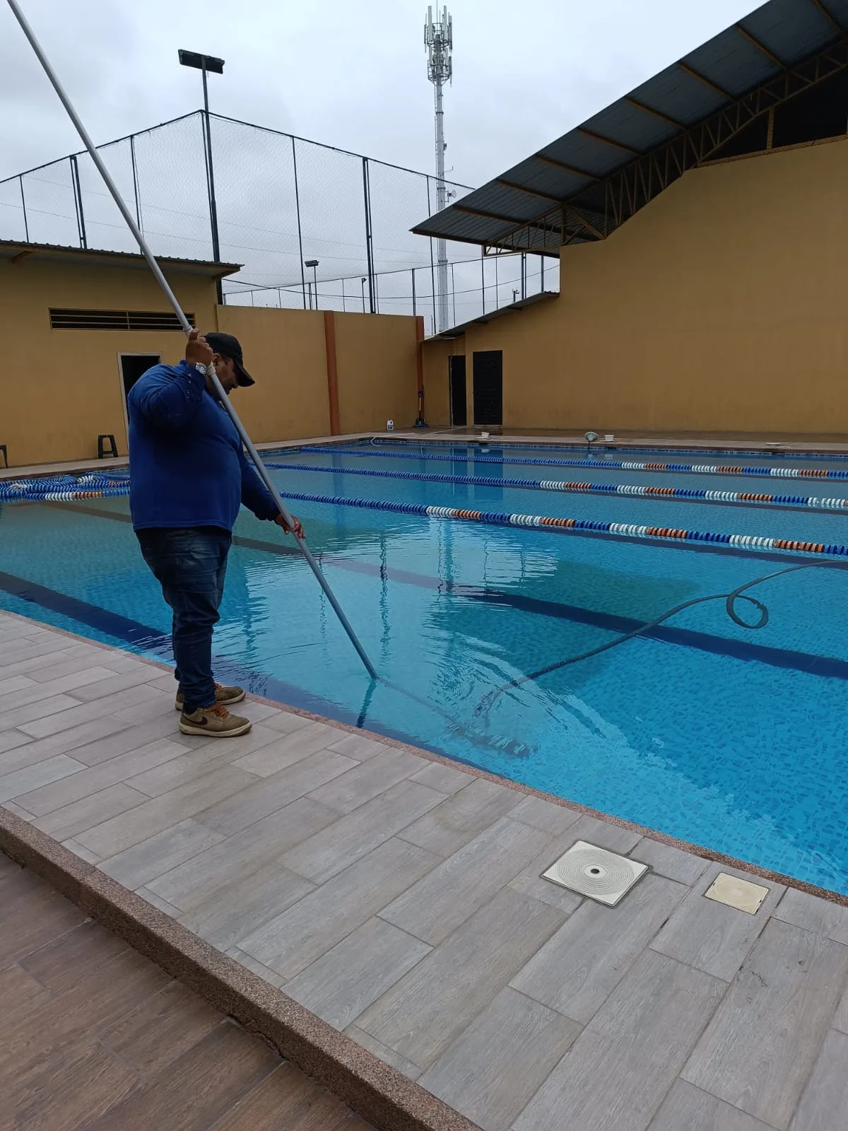 Trabajador de SolutionPlus limpiando una piscina semiolímpica con pértiga y red