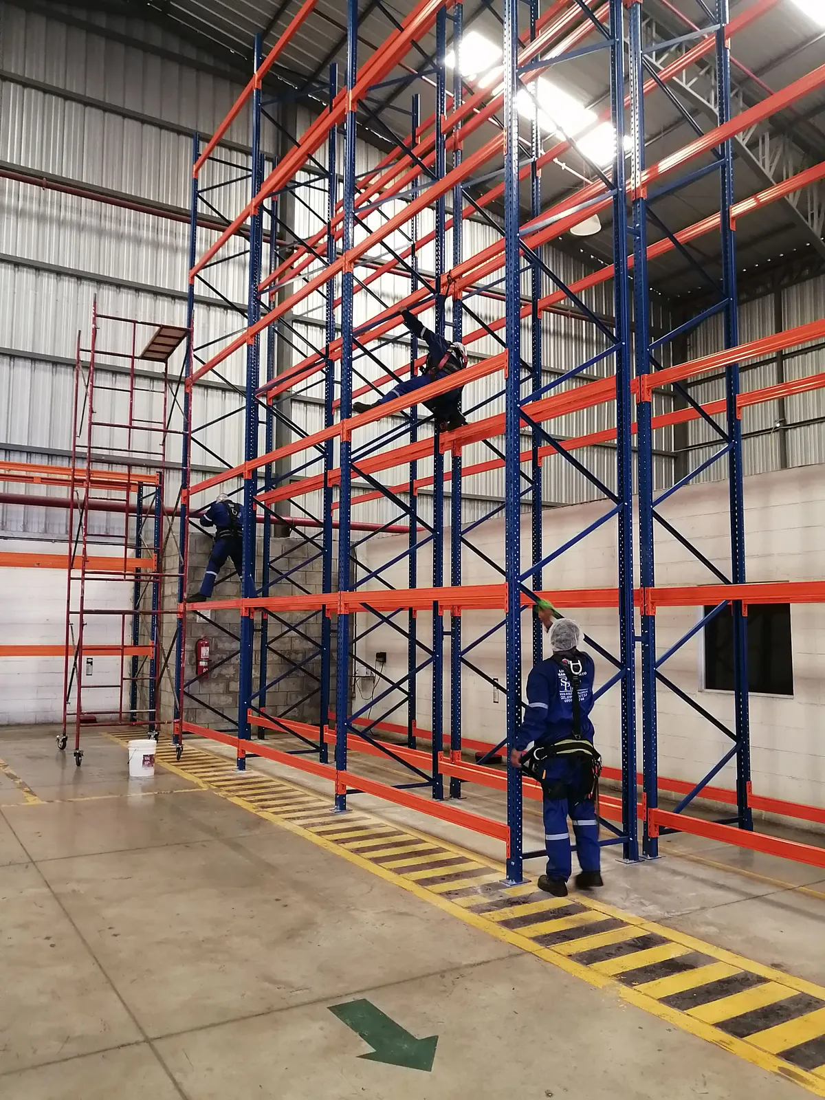 Técnicos de SolutionPlus con arnés de seguridad limpiando racks altos de una bodega