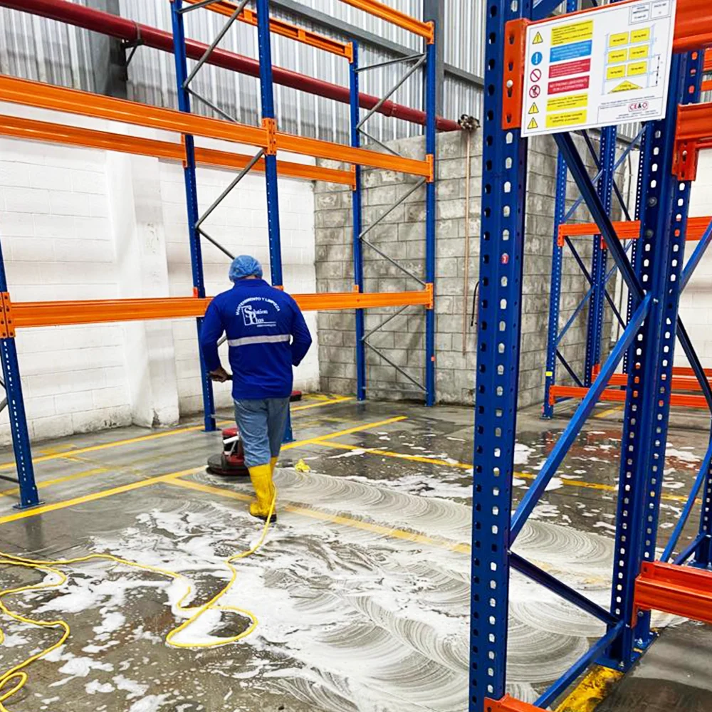 Trabajador de SolutionPlus fregando el piso de una bodega industrial entre racks metálicos