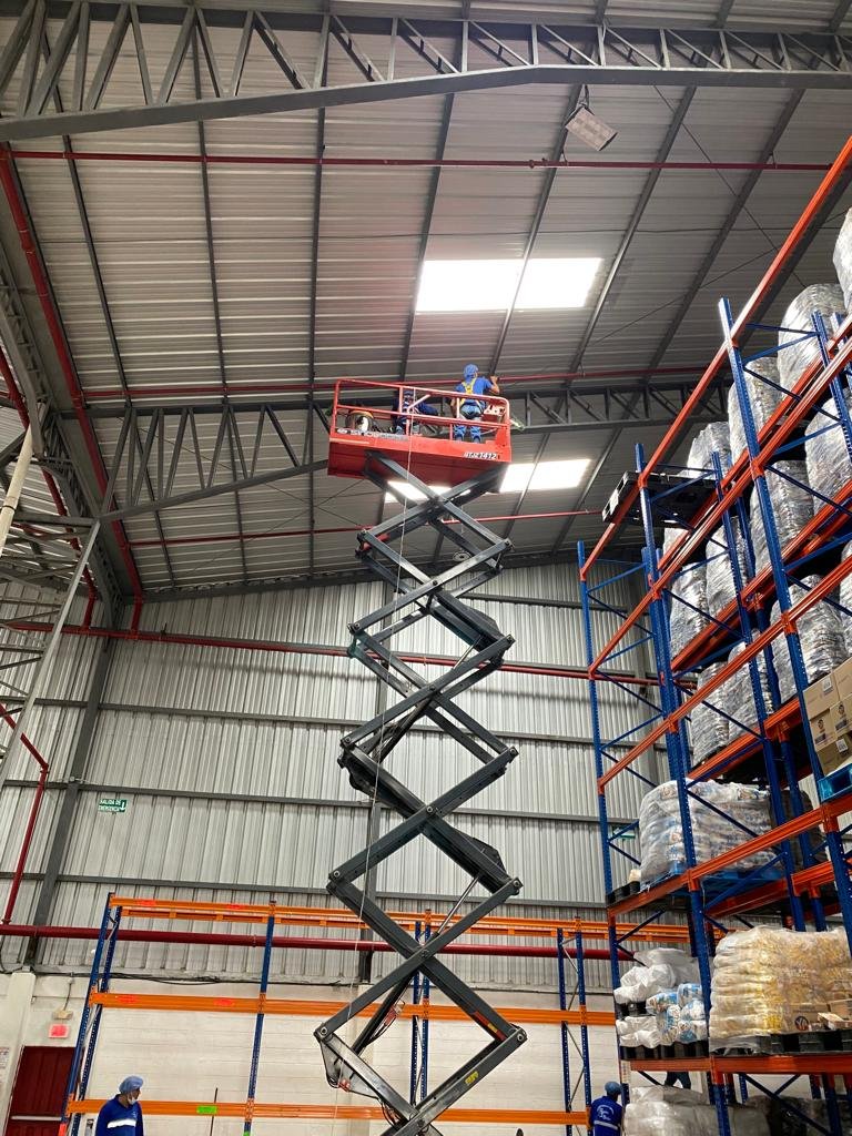 Personal de SolutionPlus limpiando la estructura del techo de una bodega industrial desde una plataforma elevadora